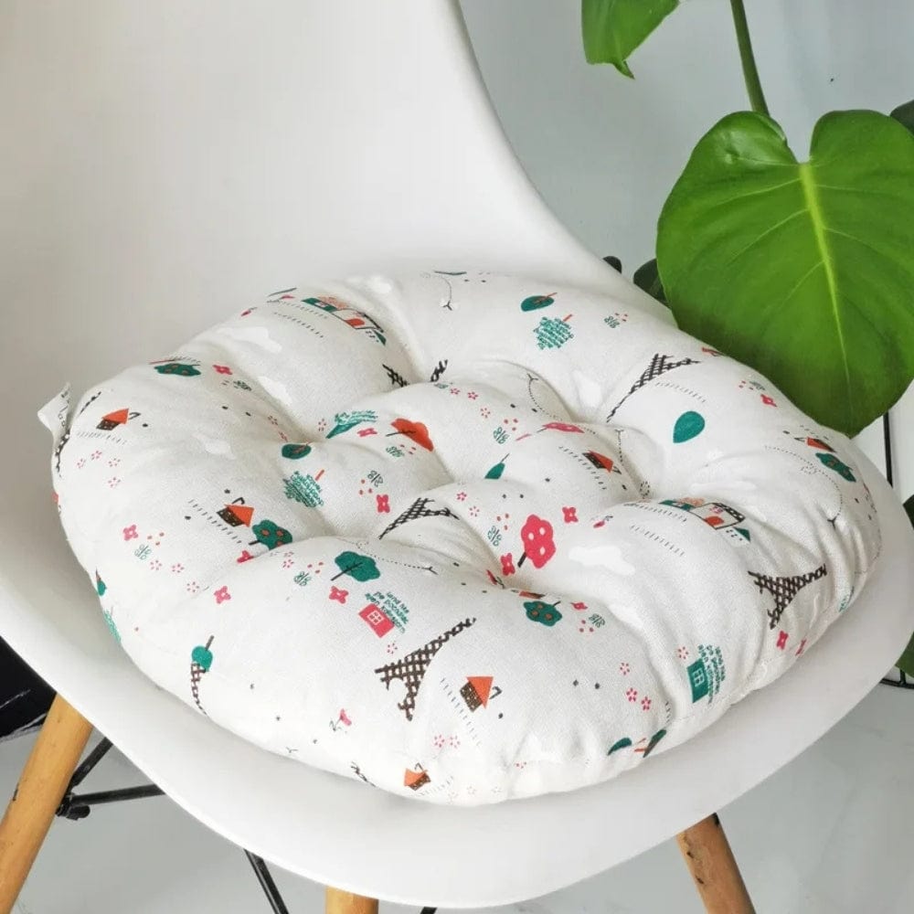 Coussin de chaise rond en tissu blanc avec motifs colorés de maisons et arbres, placé sur une chaise moderne