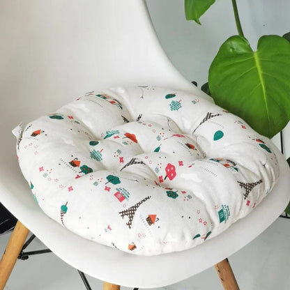 Coussin de chaise rond en tissu blanc avec motifs colorés de maisons et arbres, placé sur une chaise moderne