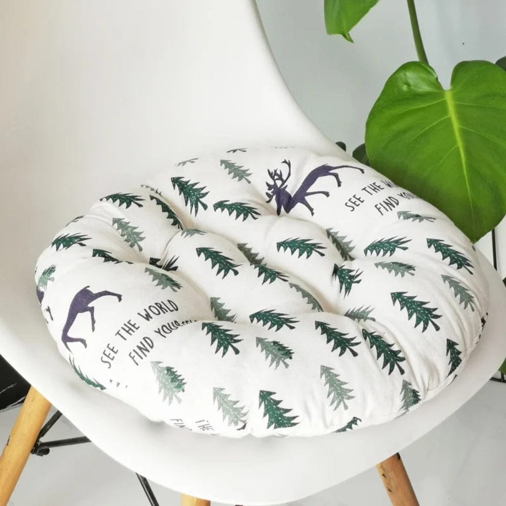 Coussin de chaise rond en tissu blanc avec motifs de sapins verts et renne violet, posé sur une chaise moderne