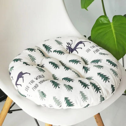 Coussin de chaise rond en tissu blanc avec motifs de sapins verts et renne violet, posé sur une chaise moderne