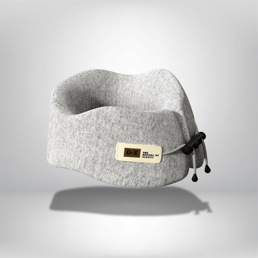 Coussin de cou en tissu gris, forme ergonomique, posé sur un fond neutre, idéal pour le voyage