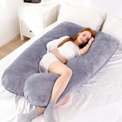 Coussin de grossesse en velours gris, posé sur un lit, offrant un soutien confortable pour le repos