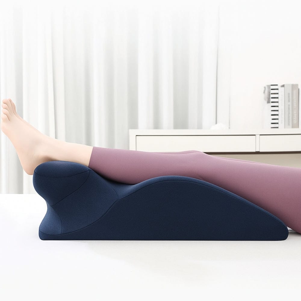Coussin de lecture en tissu bleu foncé, posé sur une table, avec des jambes reposant sur sa forme ergonomique
