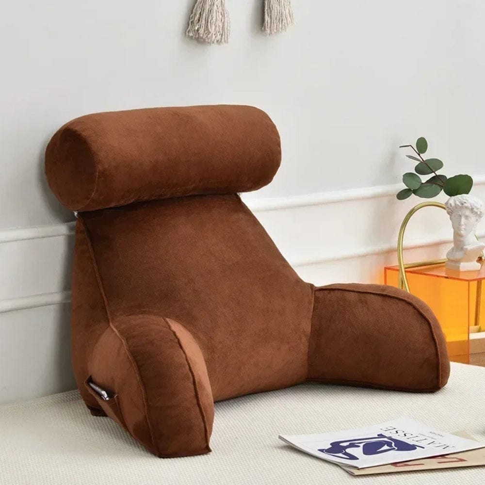 Coussin de lecture en velours marron, avec un design ergonomique, posé sur un lit décoré d'un livre