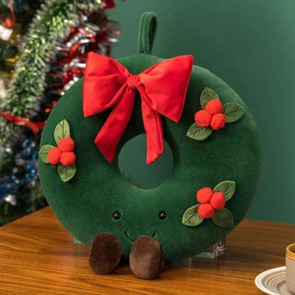 Coussin décoratif en forme de couronne verte avec un nœud rouge et des détails floraux, posé sur une table en
