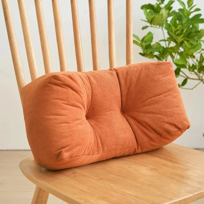 Coussin déco en velours orange, forme rectangulaire, posé sur une chaise en bois, avec un fond de plante verte