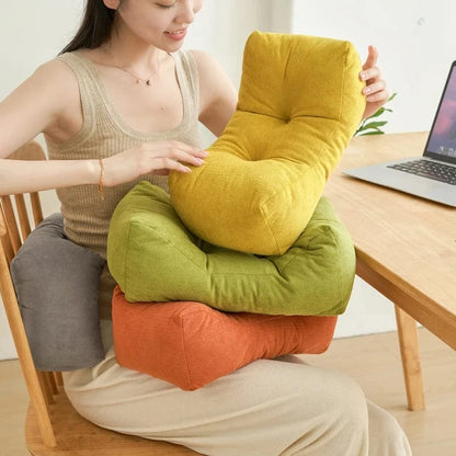 Coussins décoratifs empilés aux couleurs vives, jaune, vert et orange, sur une chaise en bois dans un intérieur moderne