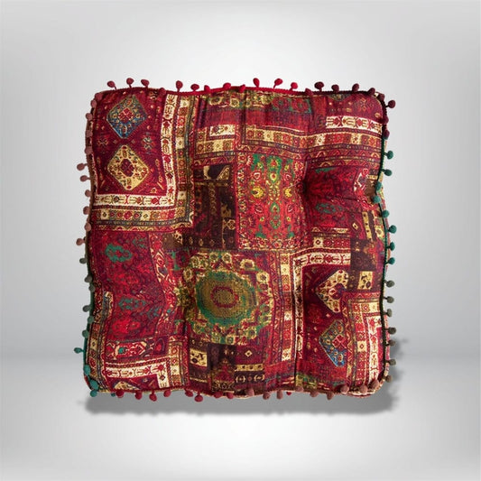Coussin de sol coloré avec motifs géométriques rouges et verts, décoré de pompons sur les bords, idéal pour un coin