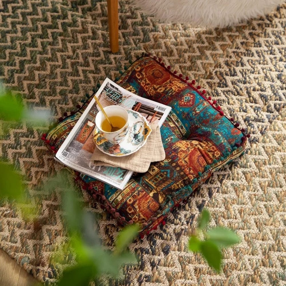 Coussin de sol coloré avec motifs orientaux, posé sur un tapis en jute, avec une tasse de thé et un