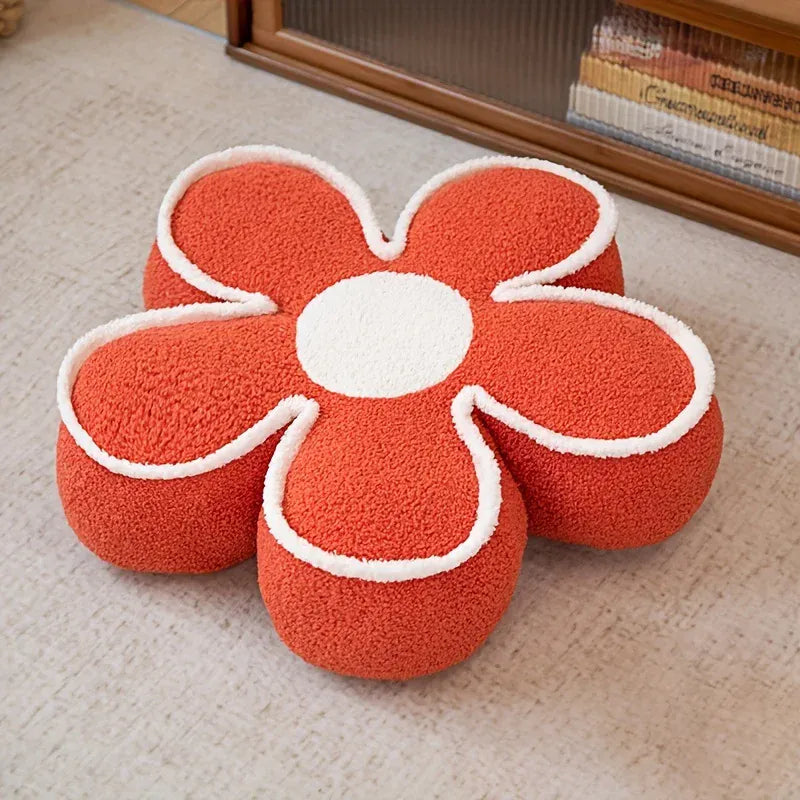 Coussin de sol en forme de fleur avec des pétales orange et un cœur blanc, posé sur un tapis