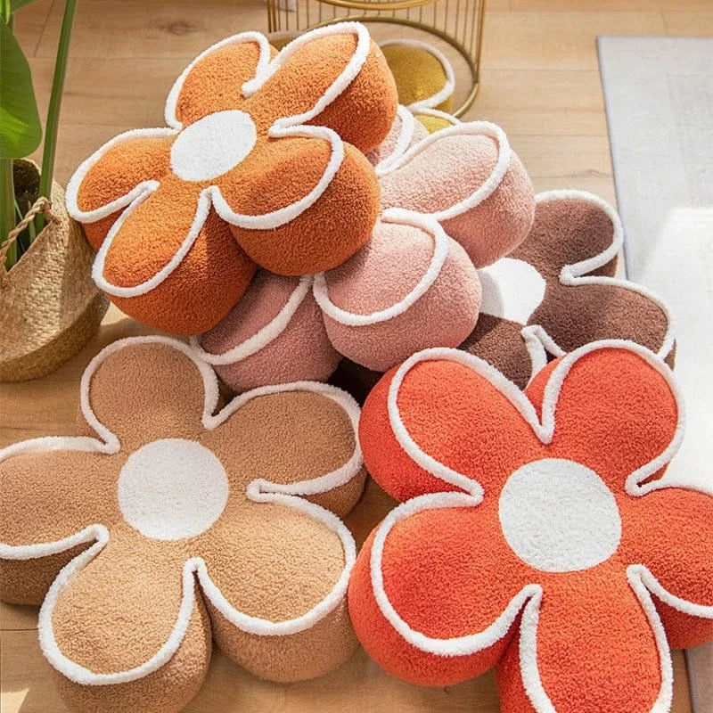 Coussins de sol en forme de fleur aux couleurs orange, rose et beige, disposés sur un sol en bois
