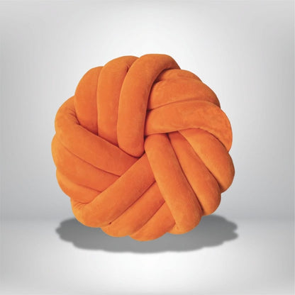 Coussin de sol en velours orange, en forme de nœud, posé sur un fond neutre