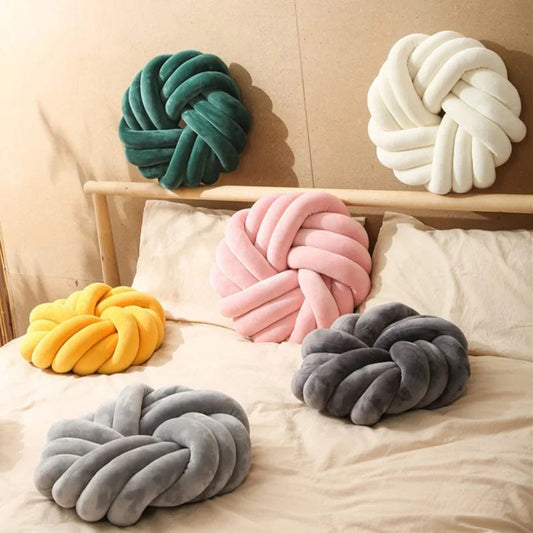 Coussins décoratifs en velours aux couleurs variées, disposés sur un lit avec des draps clairs