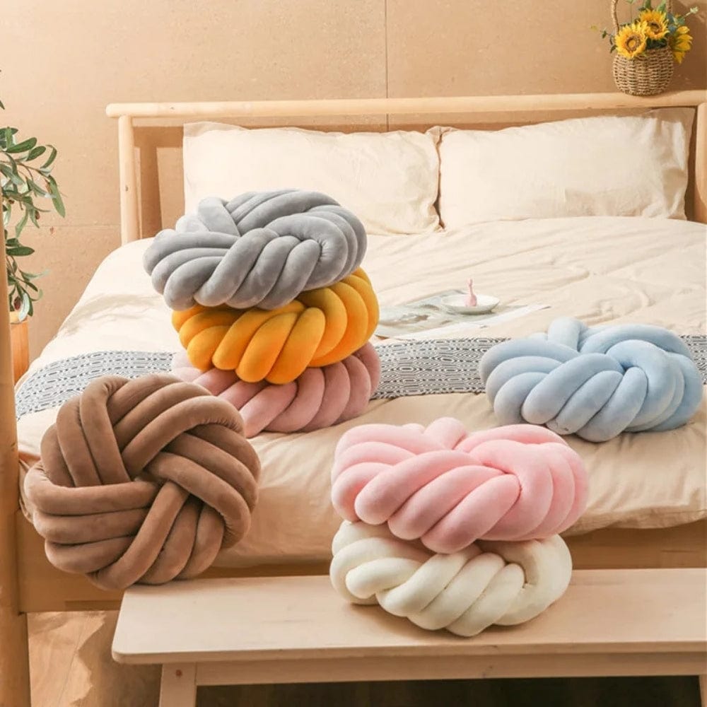 Coussins décoratifs en forme de nœud, aux couleurs pastel, posés sur un lit avec une housse de couette beige