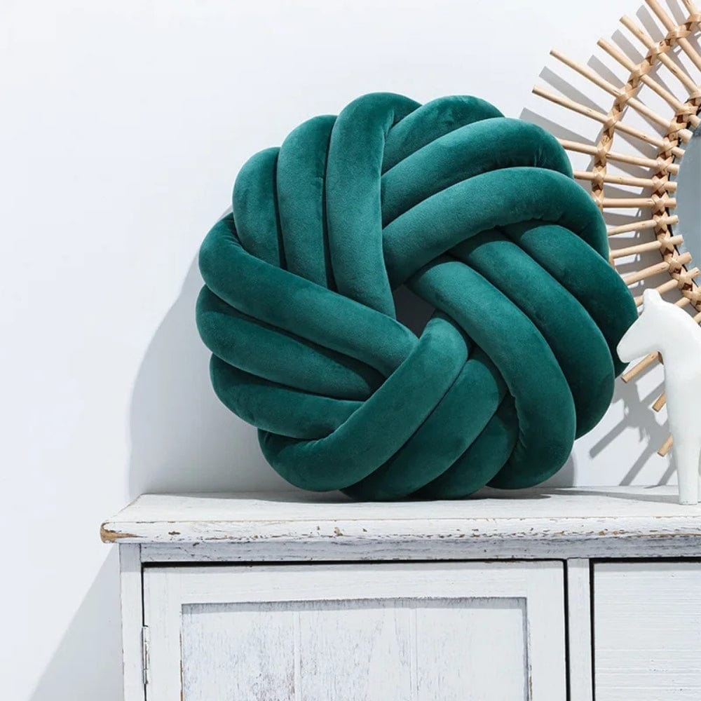 Coussin de sol en velours vert émeraude, en forme de nœud, posé sur un meuble en bois blanc
