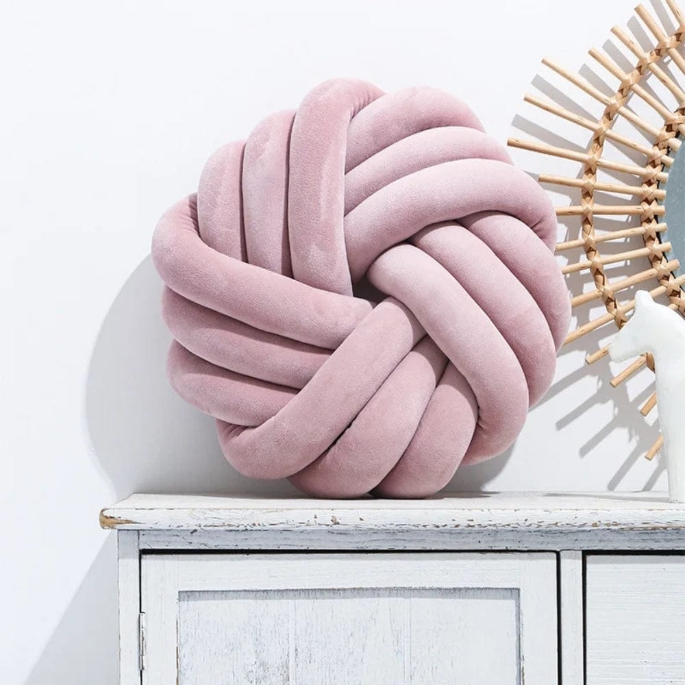 Coussin de sol en velours rose en forme de nœud, posé sur un meuble en bois blanc