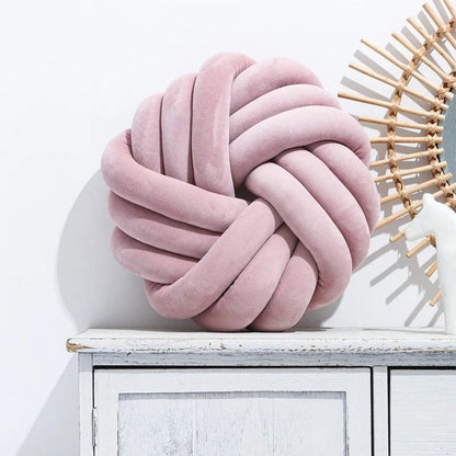 Coussin de sol en velours rose en forme de nœud, posé sur un meuble en bois blanc