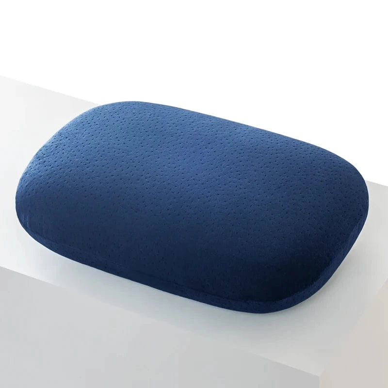 Coussin de voyage en forme rectangulaire, couleur bleu marine, matière douce et texturée, posé sur une surface blanche