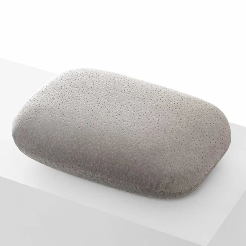 Coussin de voyage en mémoire de forme, couleur grise, texture douce et légèrement perforée, posé sur une surface blanche