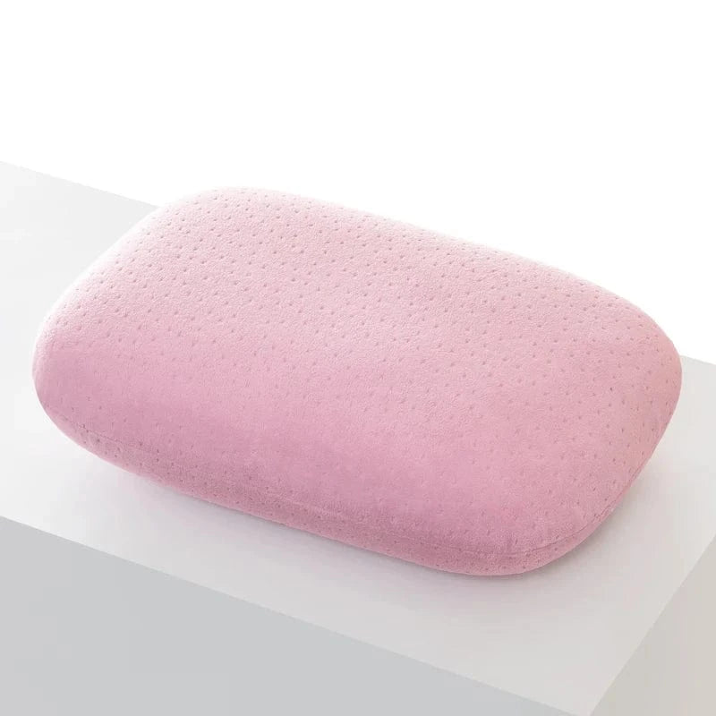 Coussin de voyage en forme rectangulaire, en velours rose, posé sur une surface blanche