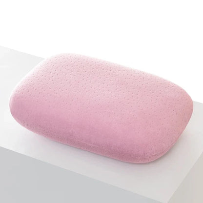 Coussin de voyage en forme rectangulaire, en velours rose, posé sur une surface blanche