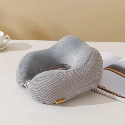 Coussin de voyage gris en velours, ergonomique, posé sur une table avec une tasse et un magazine
