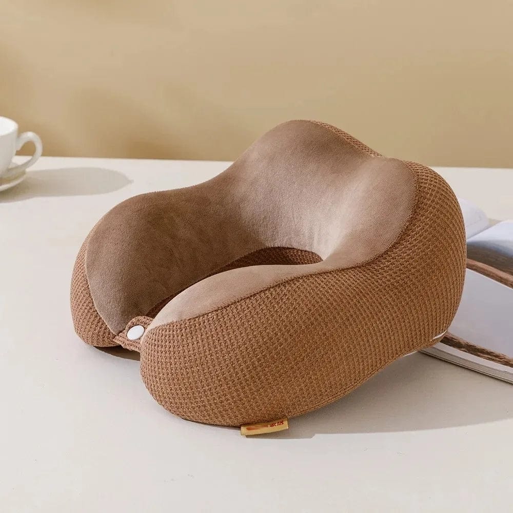 Coussin de voyage en velours marron, forme ergonomique, posé sur une table avec une tasse et un magazine