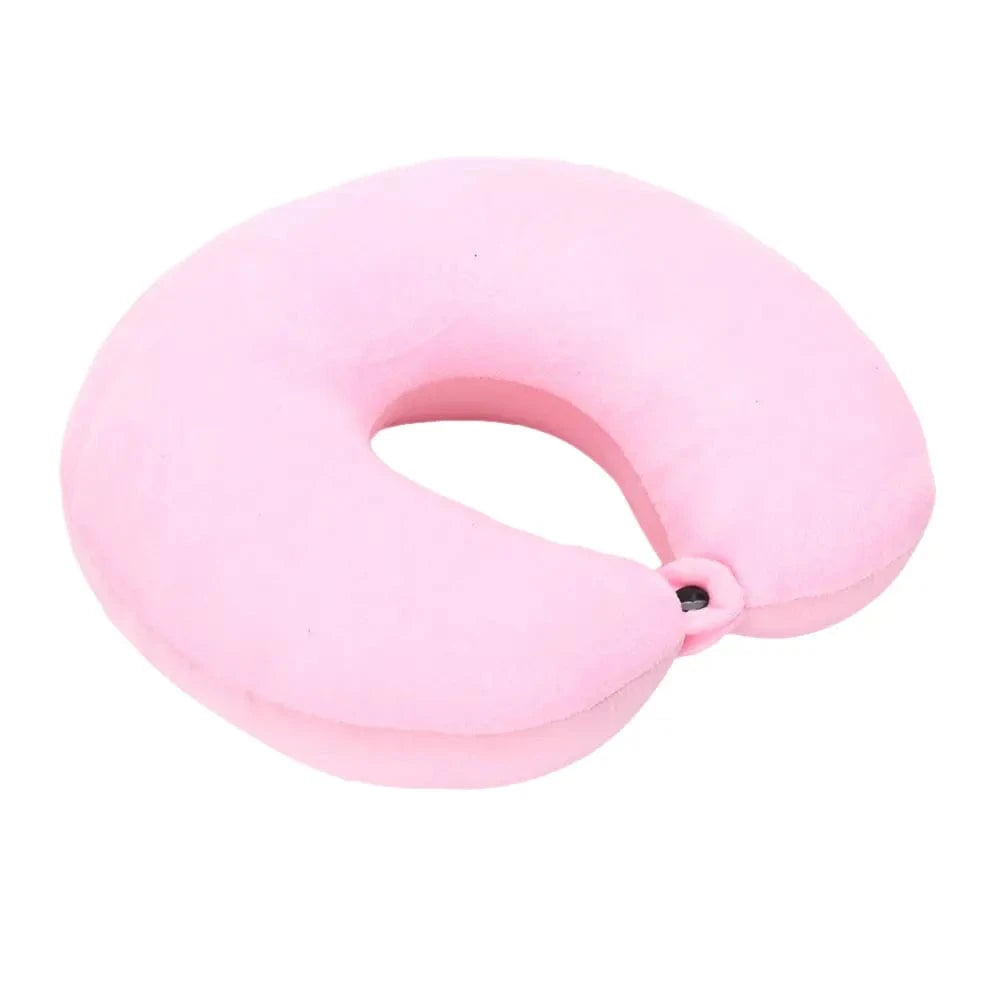 Coussin de voyage nuque en velours rose, forme ergonomique, posé sur une surface neutre