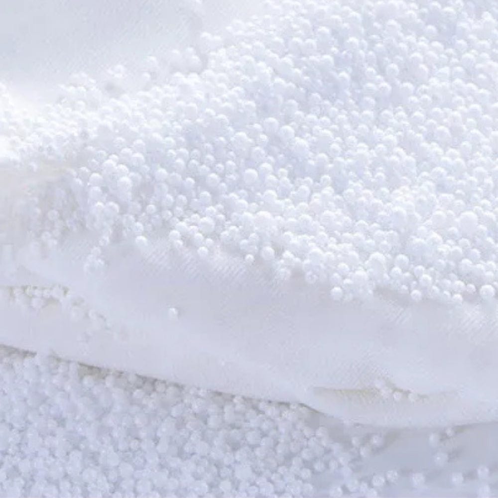 Coussin de voyage nuque en tissu blanc avec billes de rembourrage, posé sur une surface douce et lumineuse