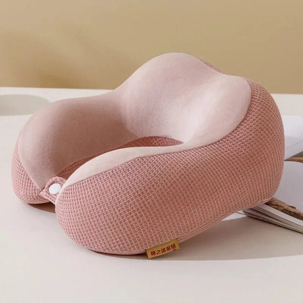 Coussin de voyage en velours rose, avec une forme ergonomique, posé sur une surface claire