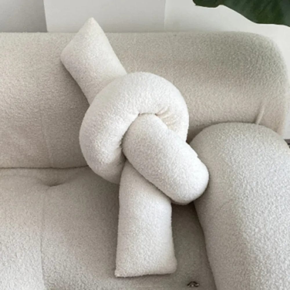 Coussin décoratif en forme de nœud, en tissu texturé blanc, posé sur un canapé beige