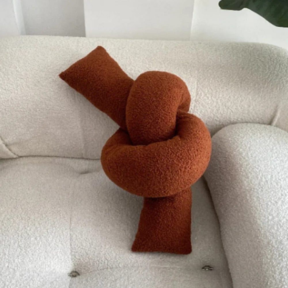 Coussin déco en forme de nœud, couleur terre cuite, posé sur un canapé blanc texturé