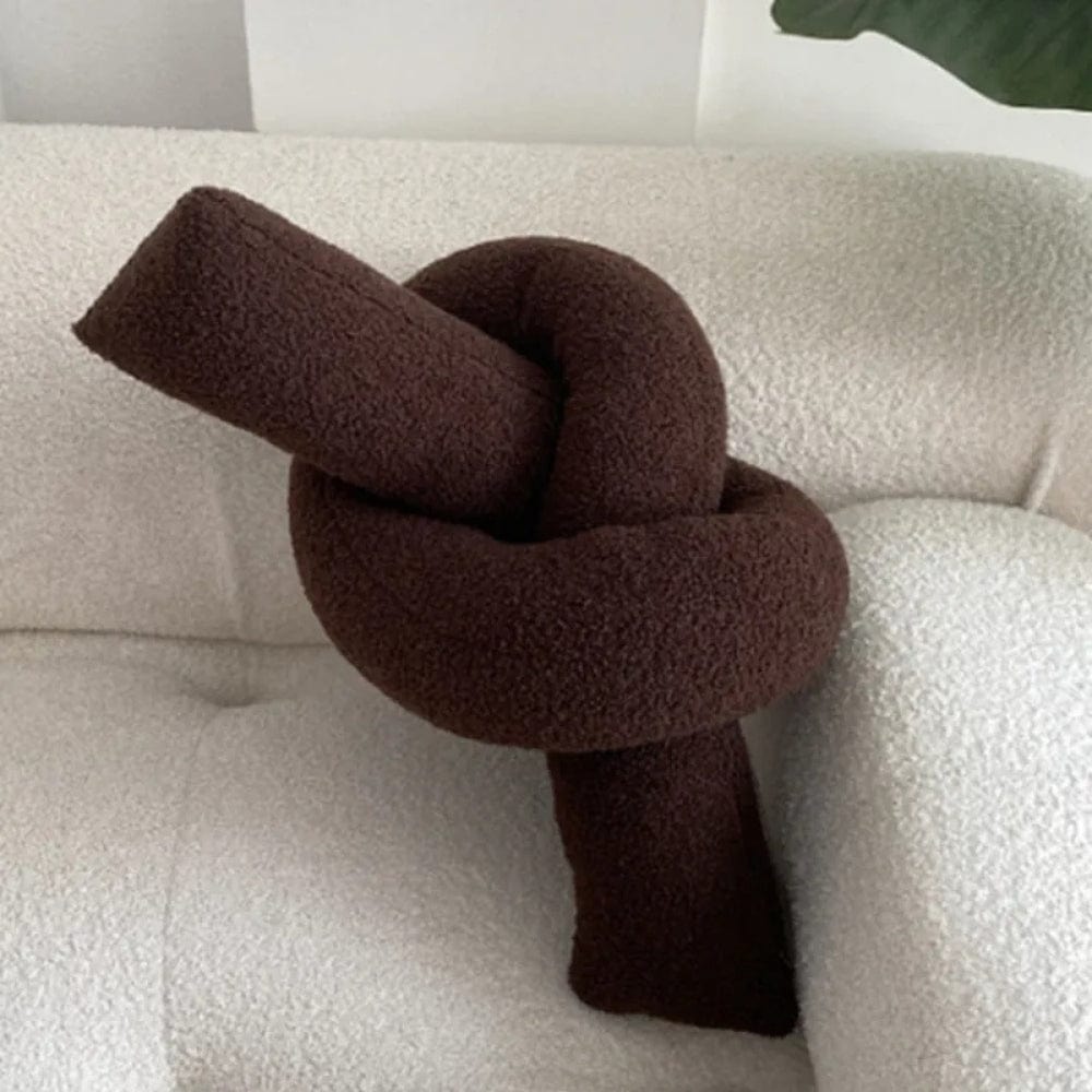 Coussin décoratif en forme de nœud, couleur marron, posé sur un canapé blanc texturé