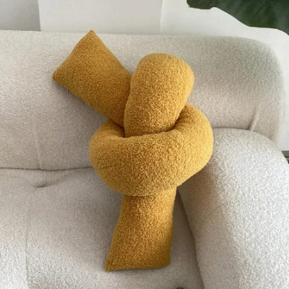 Coussin décoratif en forme de nœud, couleur jaune, en matière douce, posé sur un canapé blanc