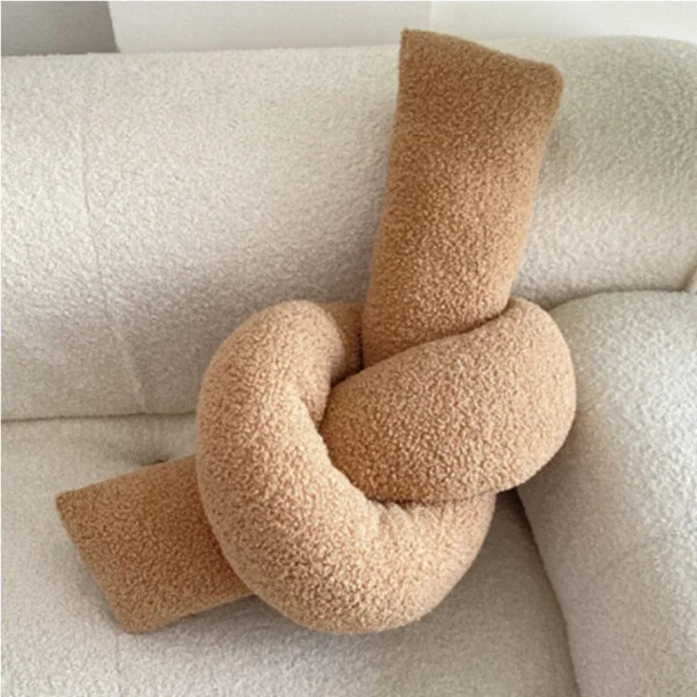 Coussin déco en forme de nœud, en matière douce et texturée, posé sur un canapé clair