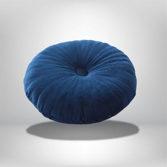 Coussin déco rond en velours bleu, avec des plis marqués, posé sur un fond neutre