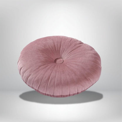 Coussin déco rond en velours rose, avec un motif plissé, posé sur un fond neutre