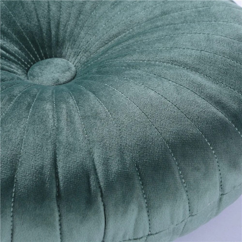Coussin déco rond en velours vert, avec des motifs côtelés, posé sur un canapé moderne