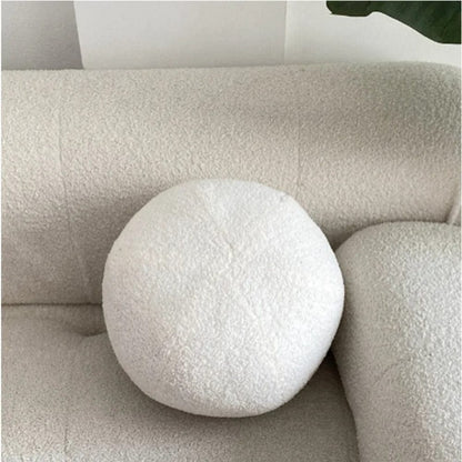 Coussin décoratif rond en tissu doux blanc posé sur un canapé beige texturé dans un salon moderne