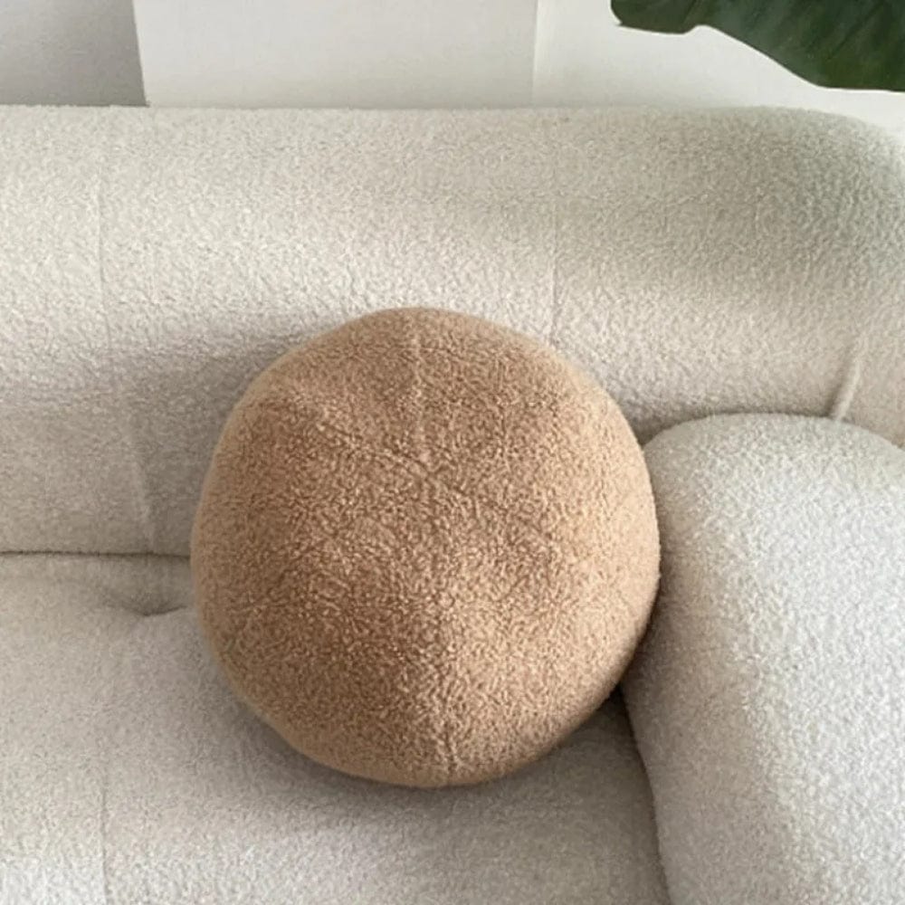 Coussin décoratif rond en tissu beige sur un canapé clair, ajoutant une touche chaleureuse au salon