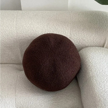 Coussin décoratif rond en tissu marron posé sur un canapé blanc texturé dans un salon moderne