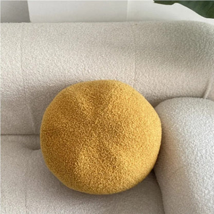 Coussin décoratif rond jaune en matière douce posé sur un canapé beige texturé dans un salon moderne