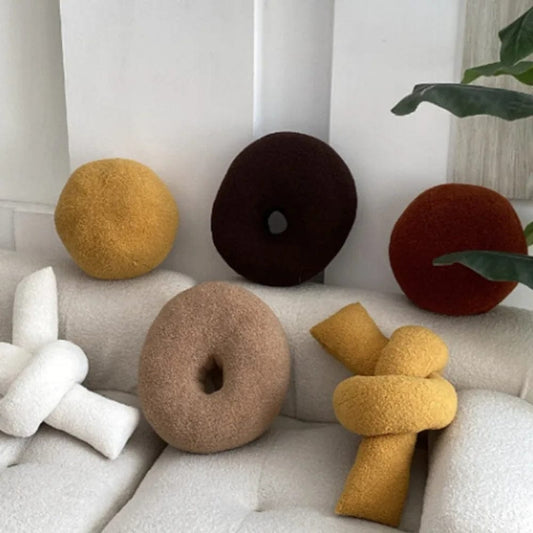 Coussins décoratifs aux formes originales et couleurs variées, posés sur un canapé moderne et élégant