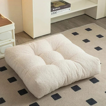 Coussin décoratif en tissu beige, forme carrée, posé sur un tapis à motifs dans un salon moderne