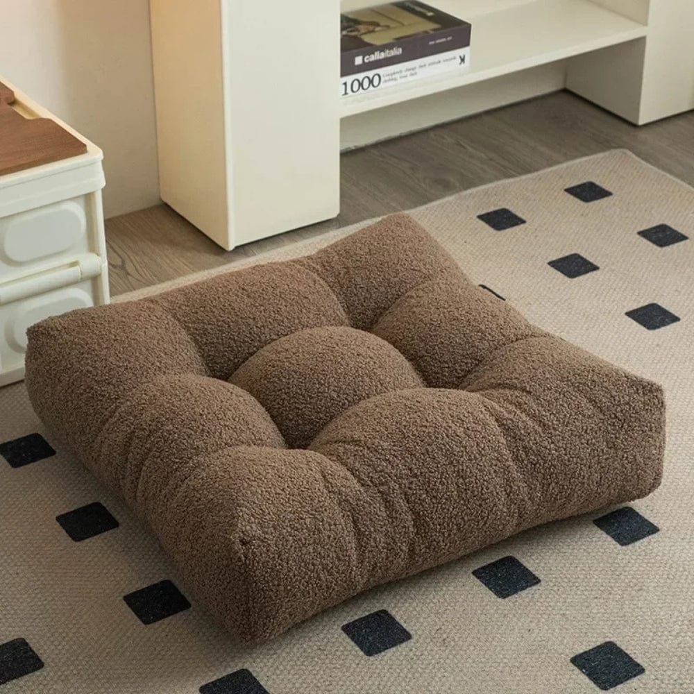 Coussin décoratif en tissu bouclé marron, placé sur un tapis, idéal pour un salon confortable