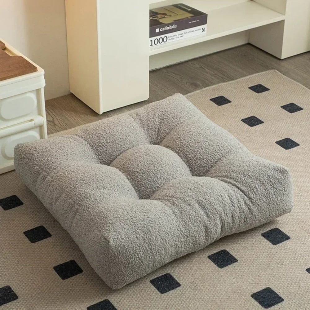 Coussin déco en tissu doux gris, carré et rembourré, posé sur un tapis à motifs dans un salon moderne