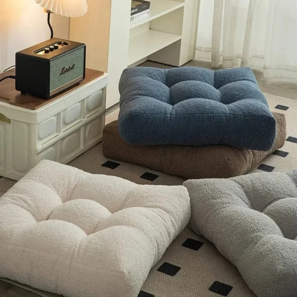 Coussins décoratifs en tissu doux, aux couleurs beige, bleu et marron, disposés sur un tapis dans un salon
