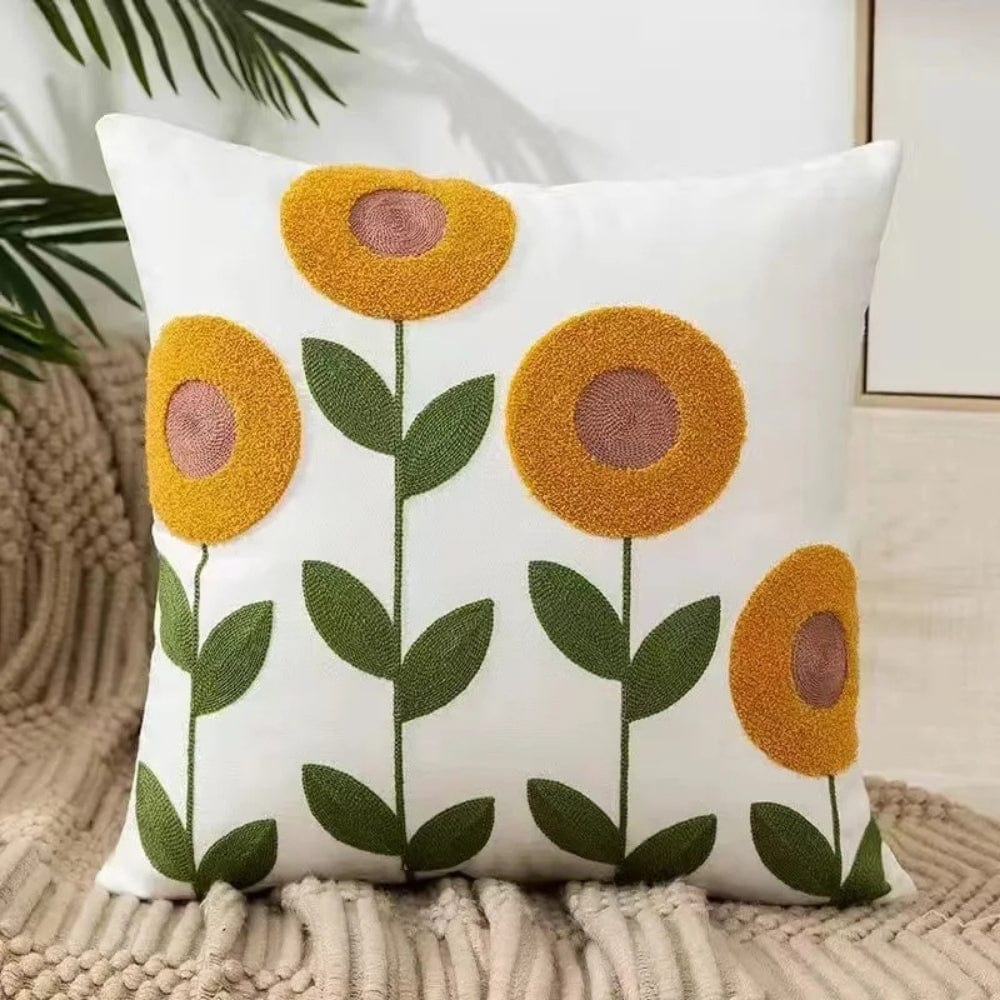Coussin déco blanc avec motifs de fleurs jaunes et vertes, posé sur un plaid beige dans un salon moderne