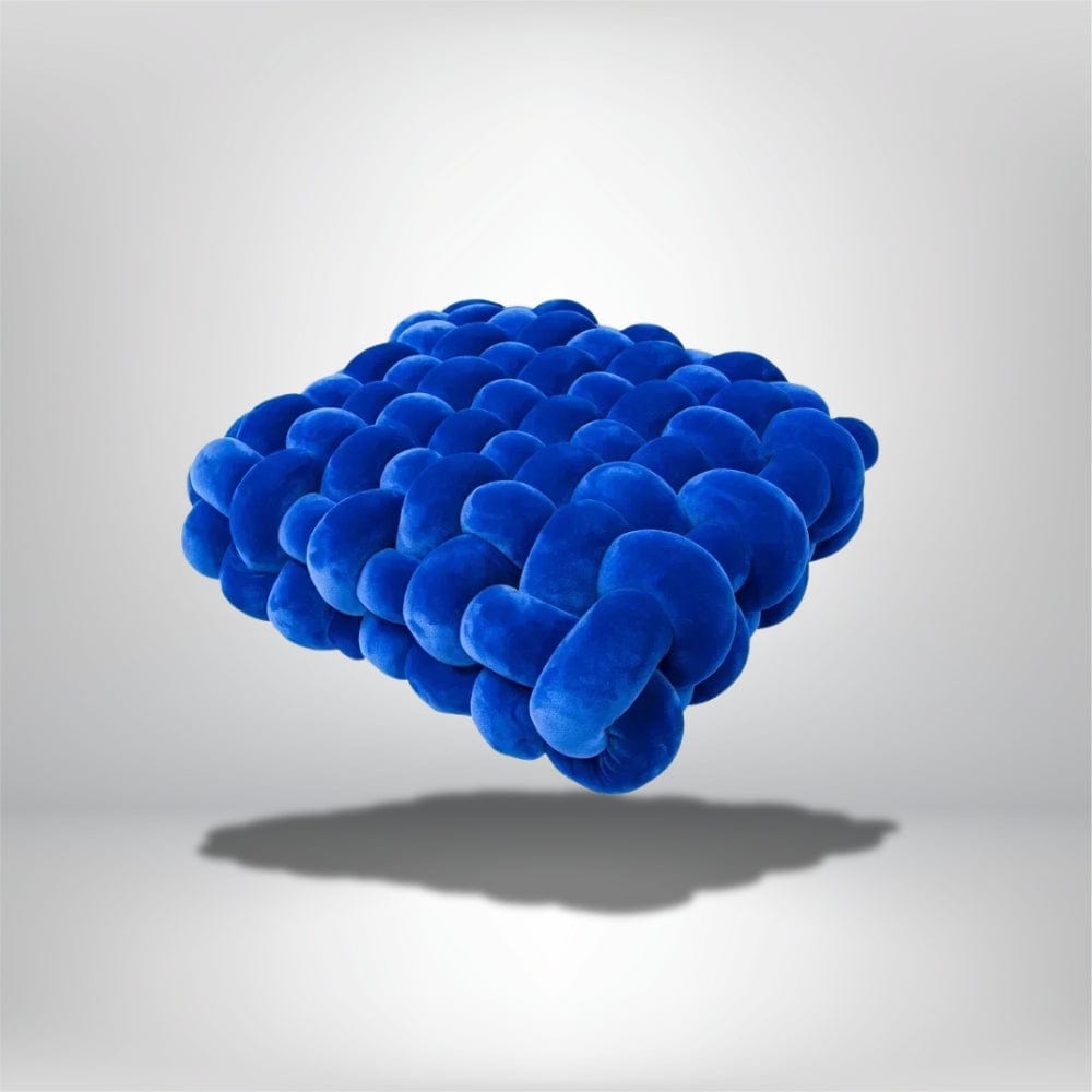 Coussin décoratif en velours bleu, au design moderne, posé sur un fond neutre