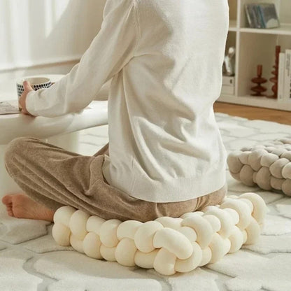 Coussin décoratif en forme de tresse, couleur crème, posé sur un tapis dans un salon moderne